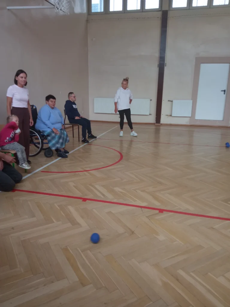 grupa 5 osób na hali. 3 osoby siedzą na wózkach/krzesłach